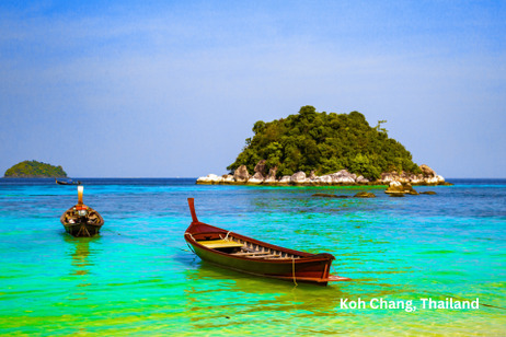 Two longtail boats float in crystal clear turquoise water near a lush green island topped with trees and rocky outcrops.