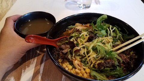 A bowl of vegan Asian food is sitting on a table with chopsticks.