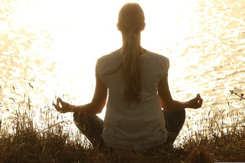 woman sitting in front of a lake meditating