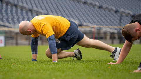 A man in a yellow shirt and blue shorts doing push ups on a grass field.