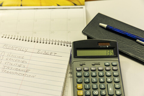 A spiral notebook with a pen and calculator on top of it.