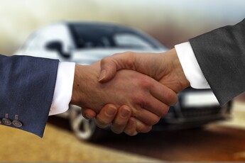 Two men shake hands with one of them wearing a suit.
