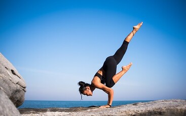 A woman is doing a hand stand on a rock.