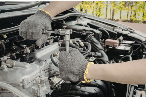 Hands in work gloves use a socket wrench on a car engine.