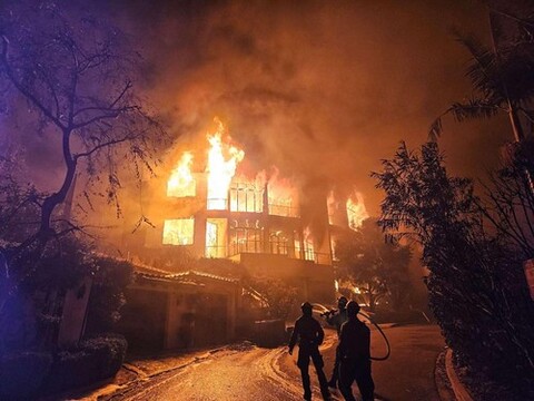 Firefighters standing in front of a building with fire in the background.