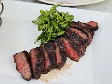 A plate with a small portion of steak has a green garnish on top.
