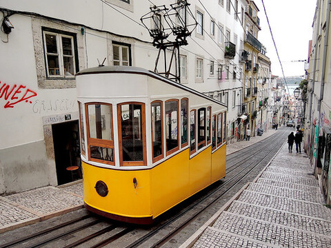 A yellow street car is traveling down a brick road.