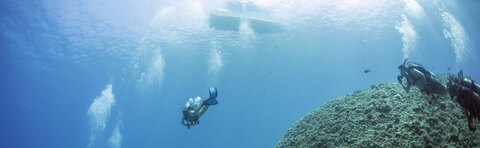 A group of divers can be seen floating on top of a rocky reef in the ocean. They seem to be enjoying their time beneath the water, observing the underwater environment and perhaps even interacting with various marine life forms. There are several people visible in the scene, indicating a group activity or expedition.