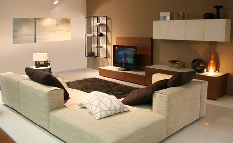 A modern living room with a large couch, a television on a stand in front of the couch, and several other items such as a vase, a clock, a bowl, a book, and a remote control.