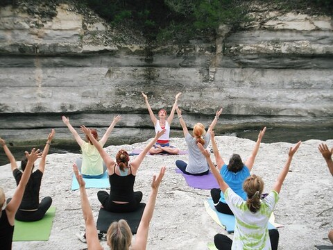 A woman with red hair is wearing a white shirt and red shorts as she poses on a yoga mat.