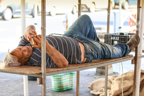 The man is lying down on a bench outside.