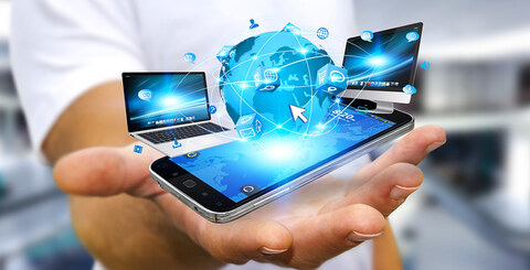A hand holding a cell phone and a laptop, with four smaller screens showing various applications.