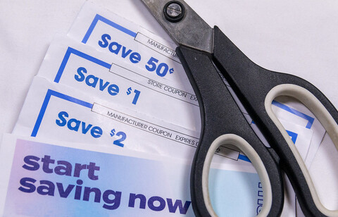 Scissors with the handles turned inside out sit atop some paper. The paper appears to be a collection of coupons with the word "save" on it.