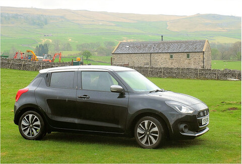 A gray car parked next to a grass field and a brick fence.