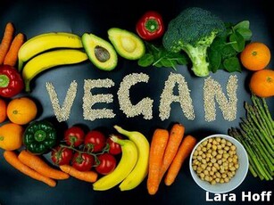 A plate of vegetables, including carrots and oranges, along with a bowl of nuts and a plate of broccoli. The word "Vegan" is written above the pile of food.