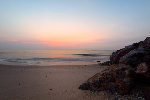 A beautiful sunset over the ocean with rocks in the foreground.