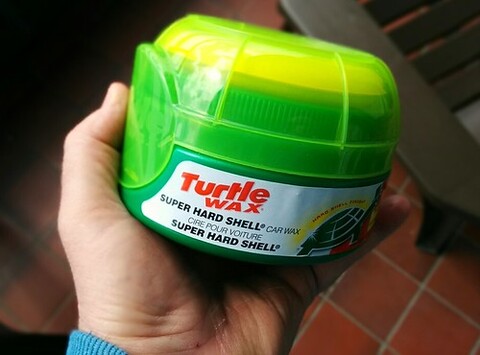 A person holds a green and yellow box with the label "Turtle Super Hard Shell!" on it.