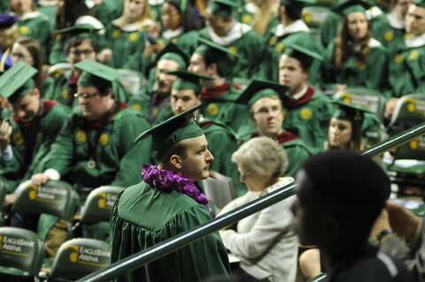 Graduating students in cap and gowns standing on stage with each other.