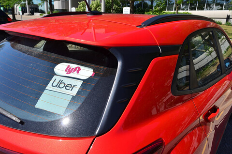 A red car with multiple American ridesharing apps in the rear window.