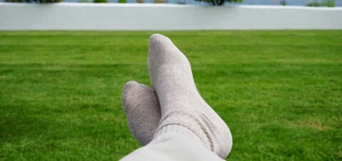 The image features a grass field with a pair of bare feet wearing white socks. The grassy field stretches out to the background, creating a serene and peaceful atmosphere.