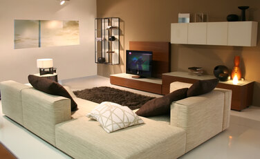 A modern living room with a large couch, a television on a stand in front of the couch, and several other items such as a vase, a clock, a bowl, a book, and a remote control.