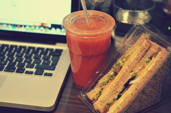 A healthy smoothie and a sandwich next to a laptop computer.